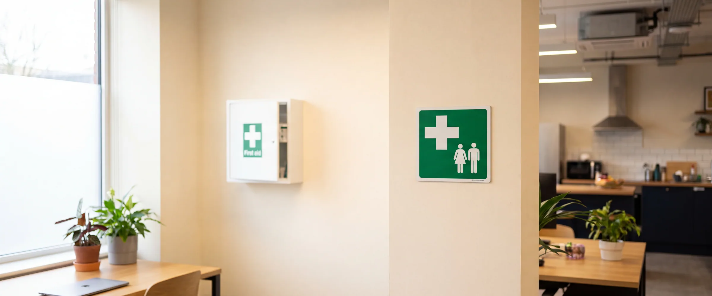 A green first aid sign beside a workplace first aid cabinet
