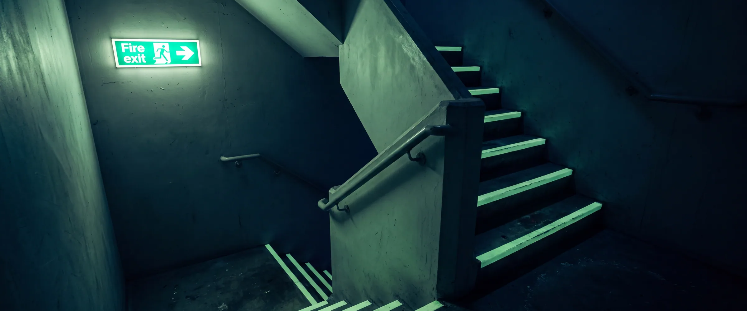 Photoluminescent exit signage and stair markings glowing in a dark stairwell