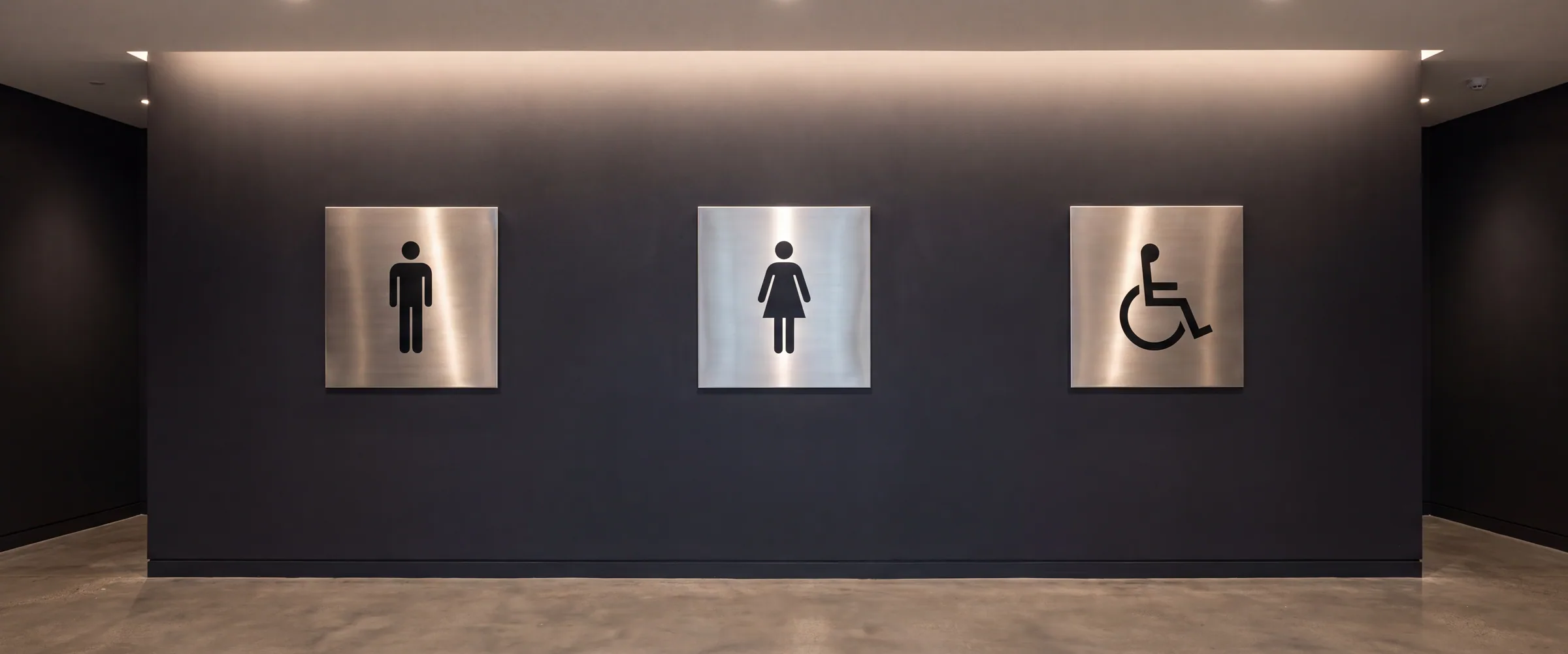 Brushed steel washroom door signs on a dark painted wall